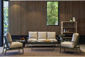 Salon contemporain avec canapé trois places et deux fauteuils beige à structure métallique, table basse et tapis. Mur habillé de panneaux muraux WoodUpp à lames verticales en bois naturel, et étagère ouverte en bois clair WoodUpp sur la droite, fenêtre laissant voir la verdure extérieure.