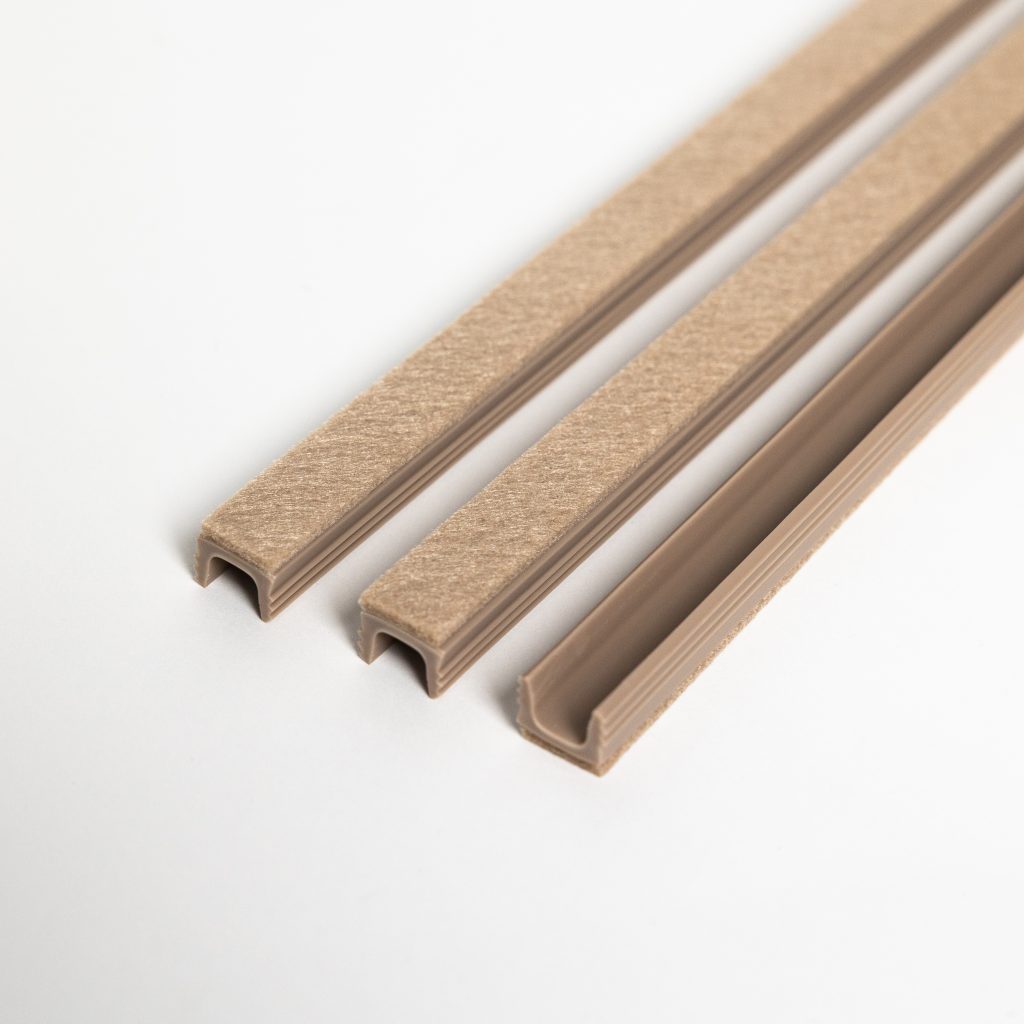 Vue rapprochée de trois profils en U WoodUpp beige : joints d'étanchéité en plastique avec gorge en U et bande feutrine autocollante sur le dessus, conçus pour se clipser sur porte ou châssis afin de réduire courants d'air, vibrations et frottements.