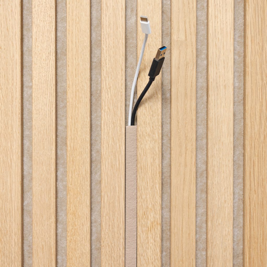 Mur acoustique WoodUpp composé de lattes fines en chêne clair séparées par un feutre gris, avec une gorge verticale pour câbles. Un cache étroit assorti laisse sortir deux câbles : un USB‑A noir et un câble blanc Lightning, illustrant la finition et la gestion des câbles WoodUpp.