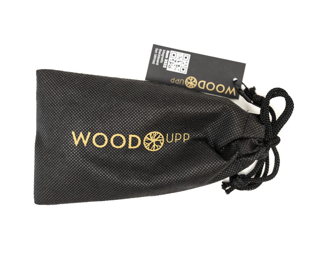 Sacoche noire à cordon WoodUpp en tissu texturé avec logo doré "WOODUPP" et motif circulaire rappelant une roue en bois, accompagnée d'un petit tag noir portant un QR code et le nom WoodUpp; cordons tressés noués, image sur fond blanc.