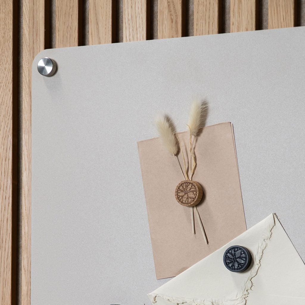Panneau magnétique WoodUpp fixé sur lambris clair, affichant une carte kraft et une enveloppe maintenues par des aimants WoodUpp ronds gravés — un aimant bois clair au motif organique sur la carte et un aimant foncé sur l'enveloppe, détails texturés et finition naturelle.